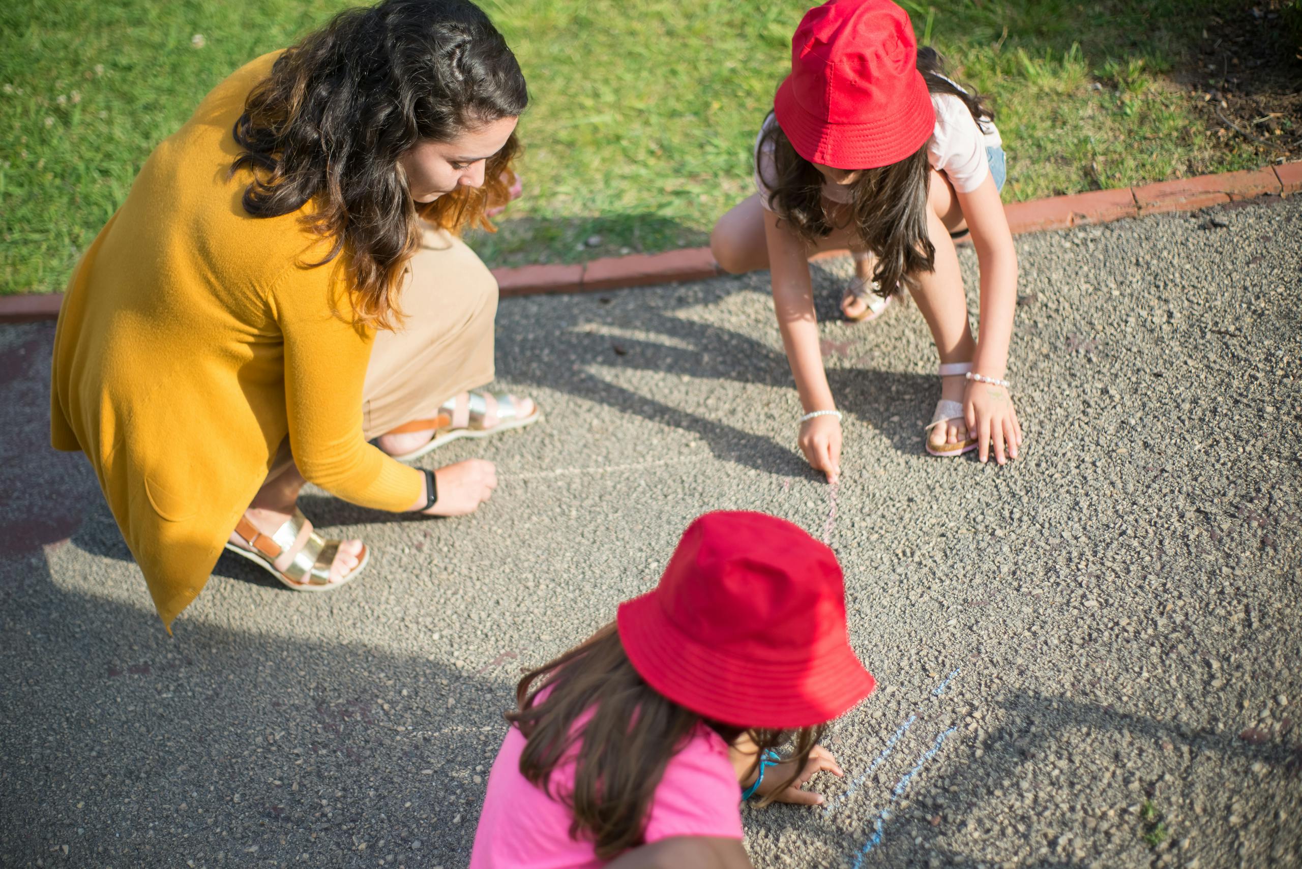 A nanny and two children drawing together on the pavement outdoors in Portugal.