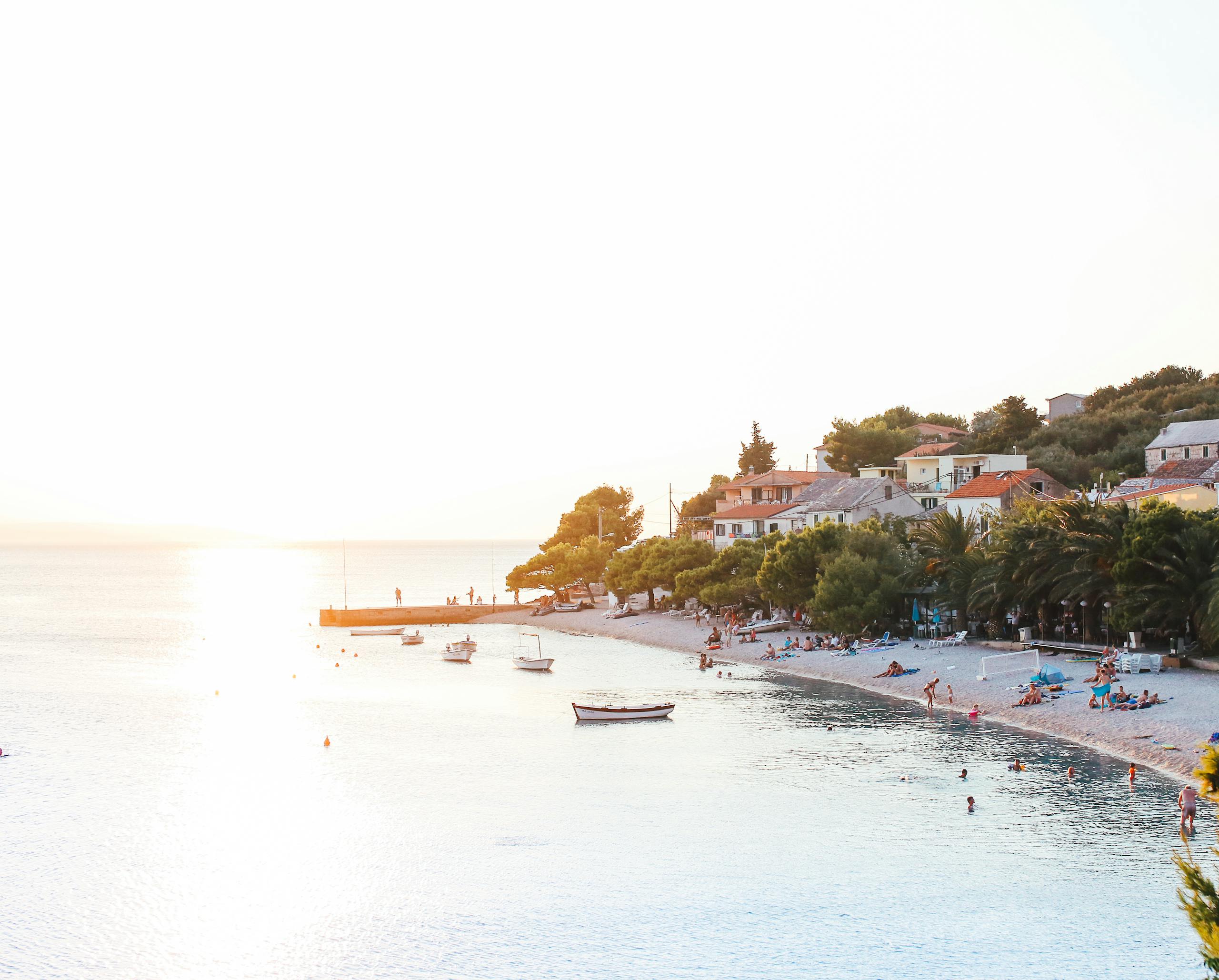 A serene beach scene with boats and visitors enjoying a summer sunset.