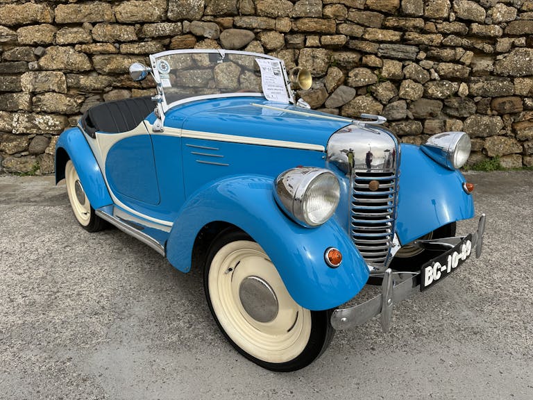 Charming vintage blue convertible car parked by a rustic stone wall in Silveira, Portugal.