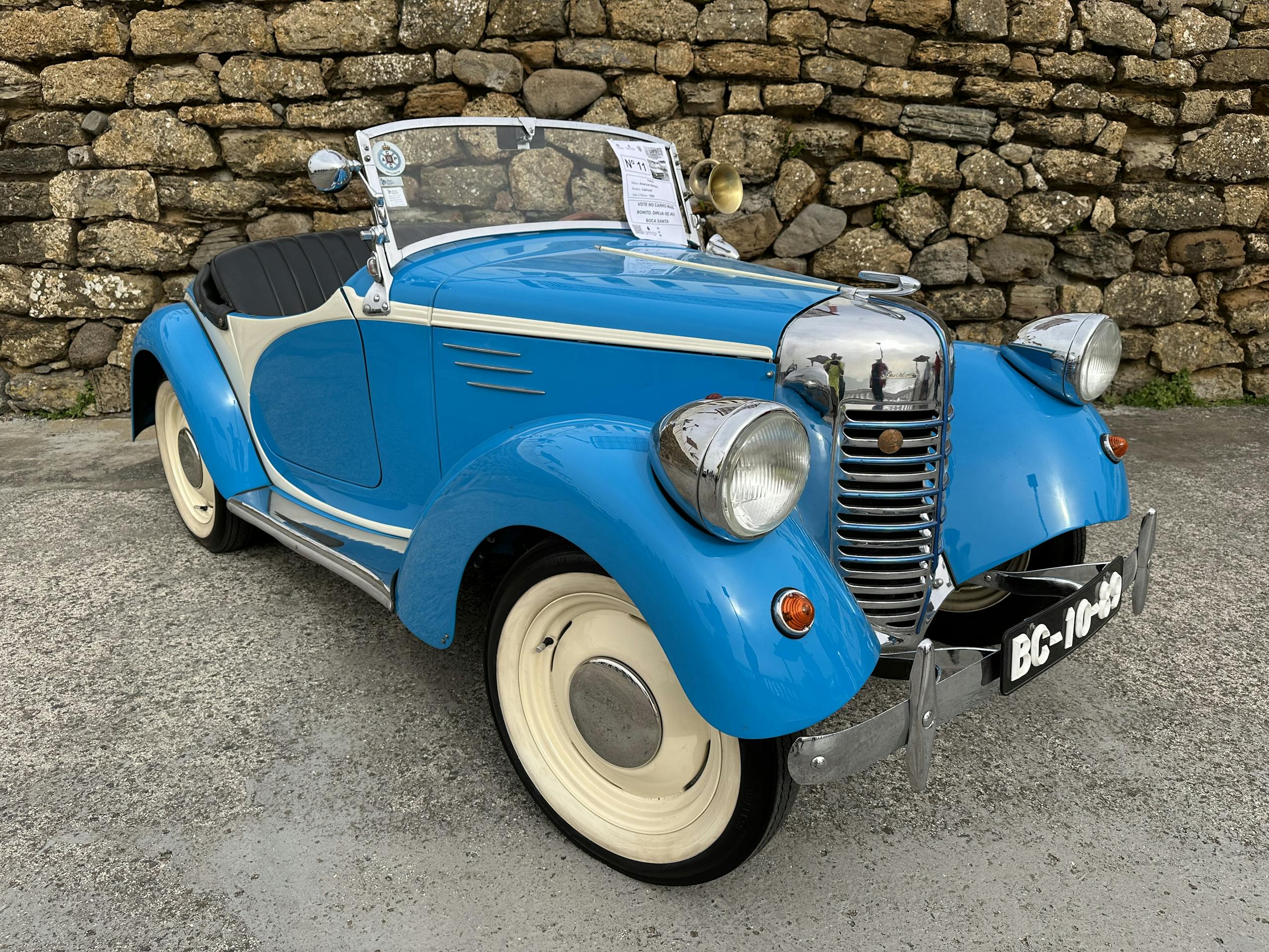 Charming vintage blue convertible car parked by a rustic stone wall in Silveira, Portugal.